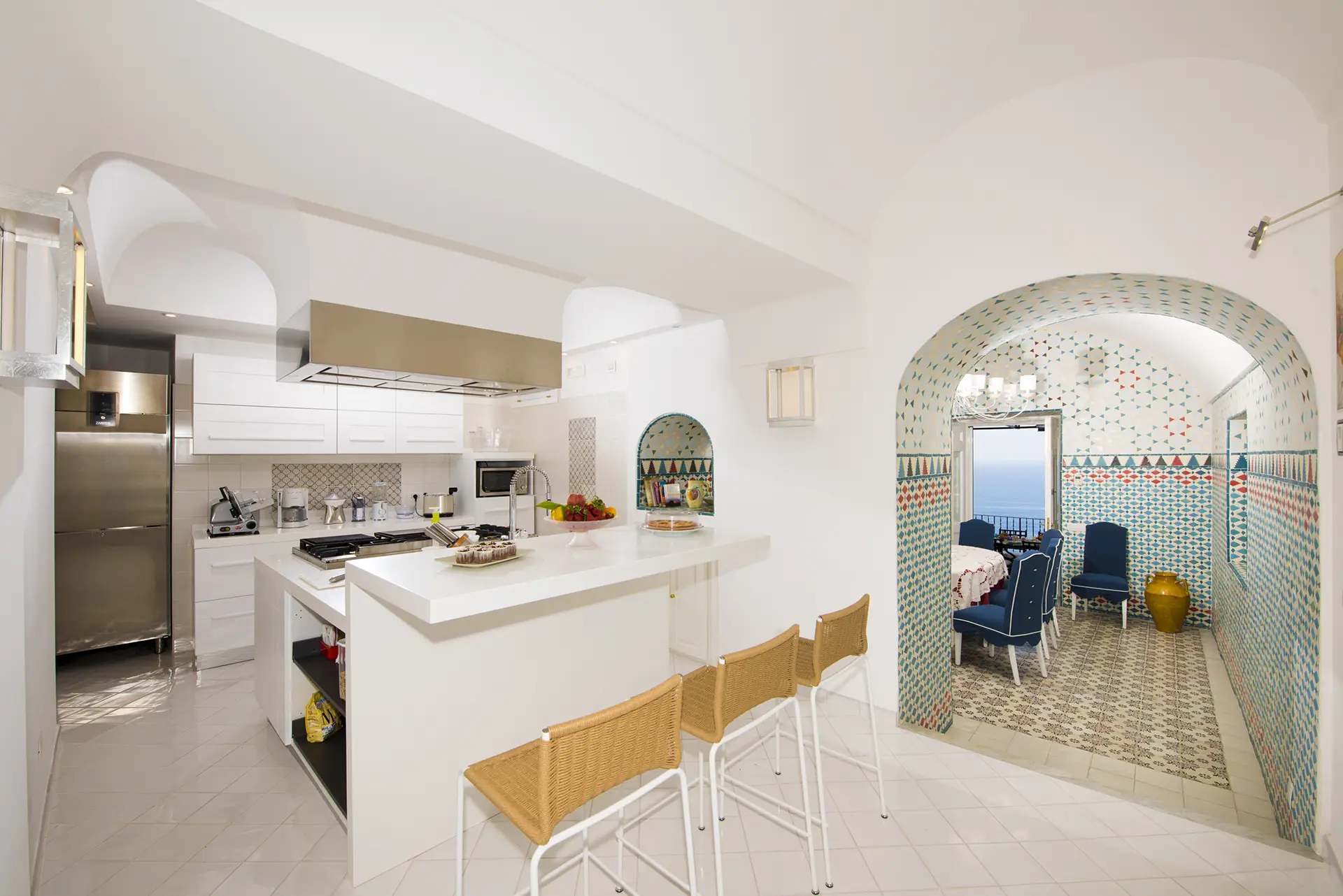 Cucina moderna con arredi bianchi e zona pranzo piastrellata colorata affacciata sul mare.