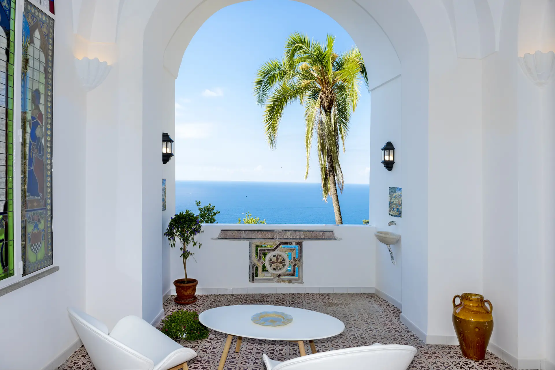 Arco bianco con vista sul mare azzurro e palma, decorato con mobili moderni ed elementi artistici.