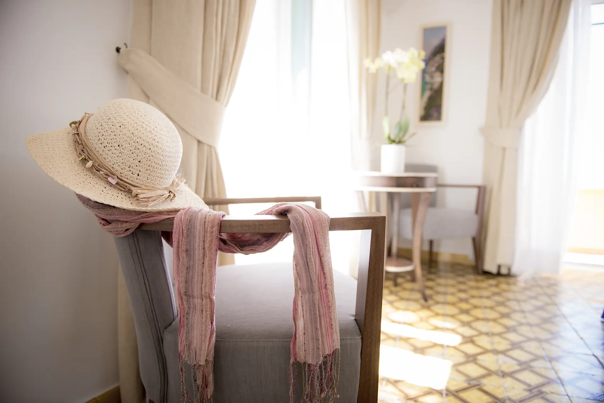 Interno luminoso con una sedia su cui sono poggiati un cappello di paglia e una sciarpa rosa.