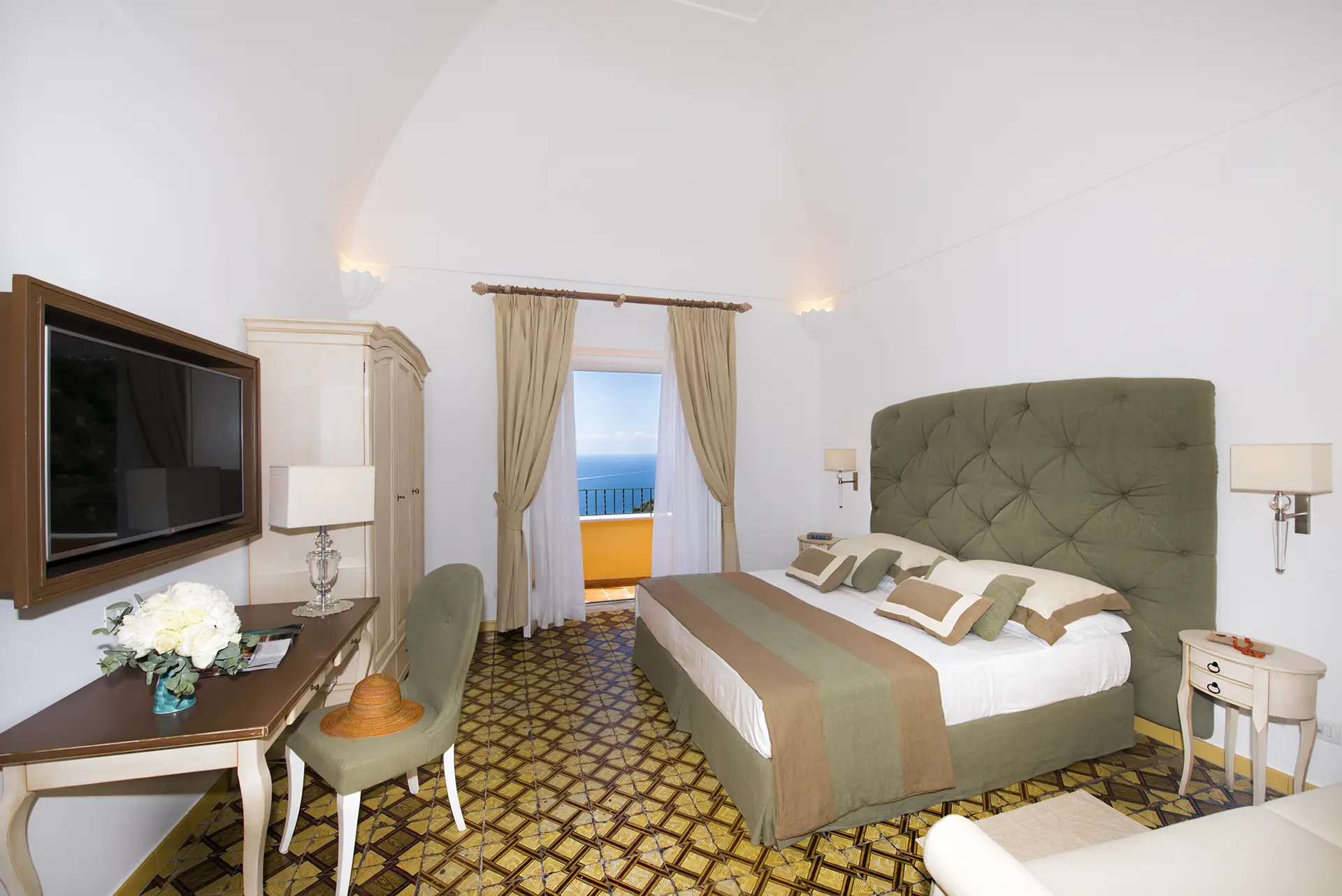 Camera da letto elegante con vista sul mare attraverso un balcone, arredo raffinato e dettagli beige e verdi.