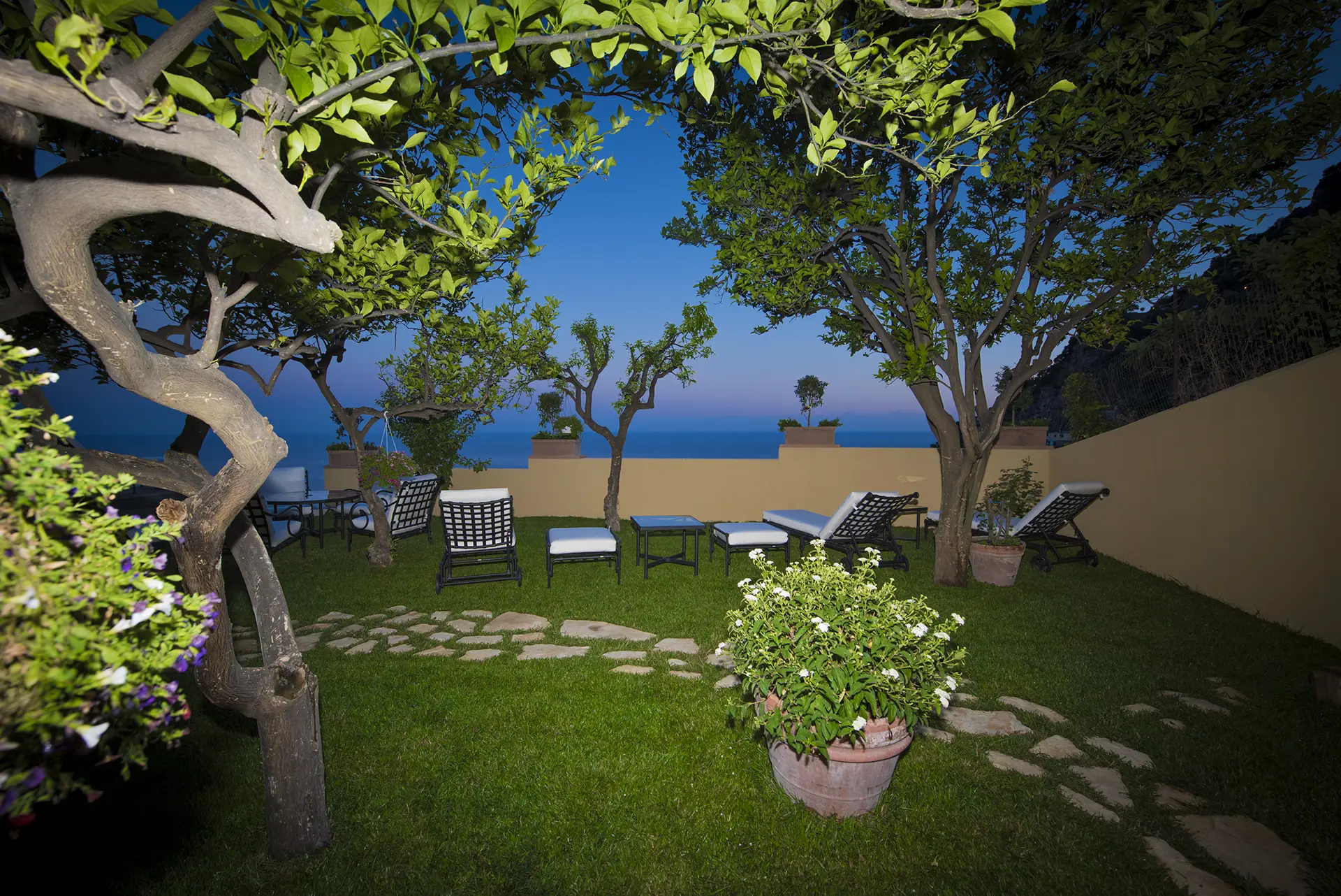 Giardino con mobili da esterno e vista mare al tramonto.