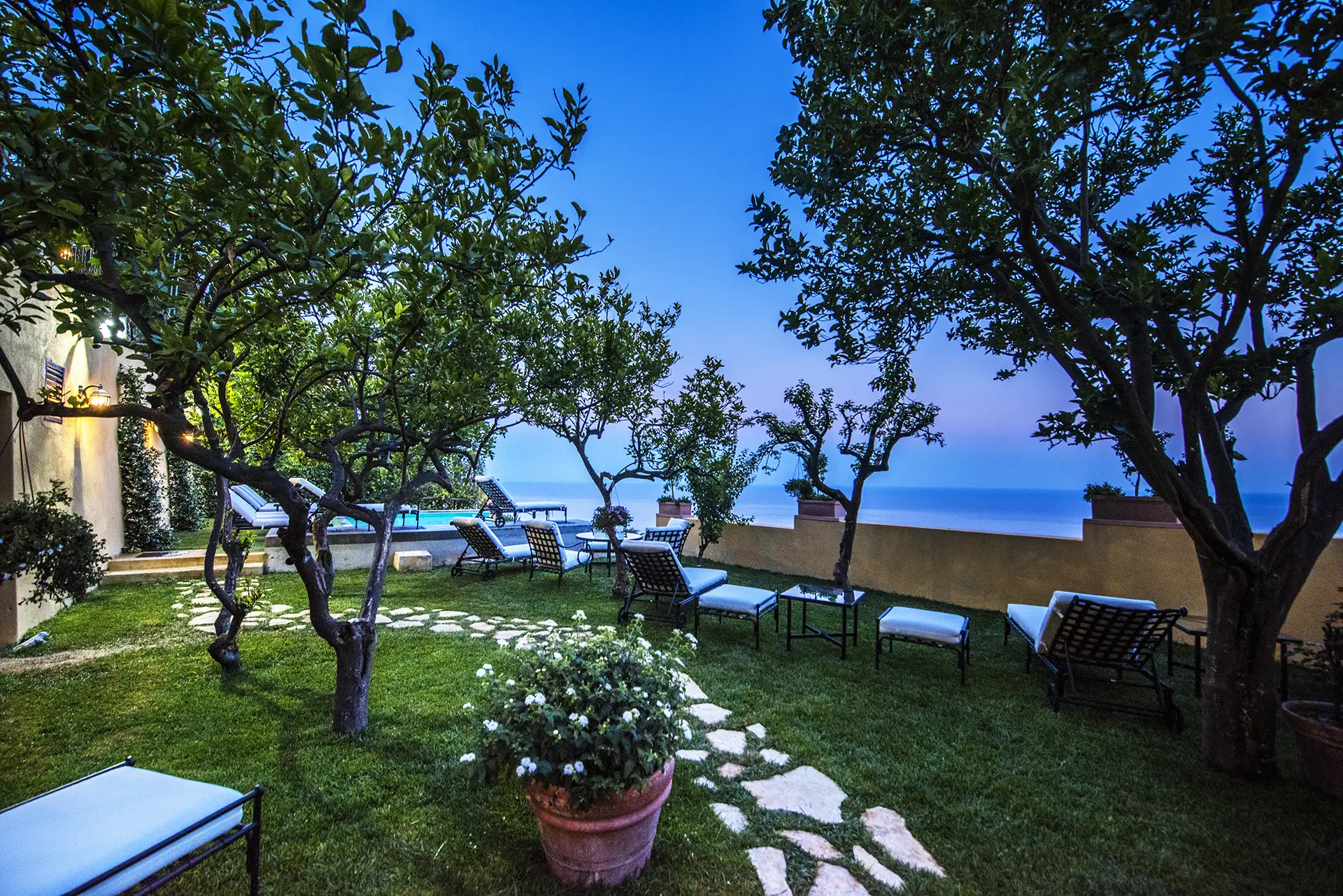 Giardino con sedie a sdraio e vista sul mare al tramonto.