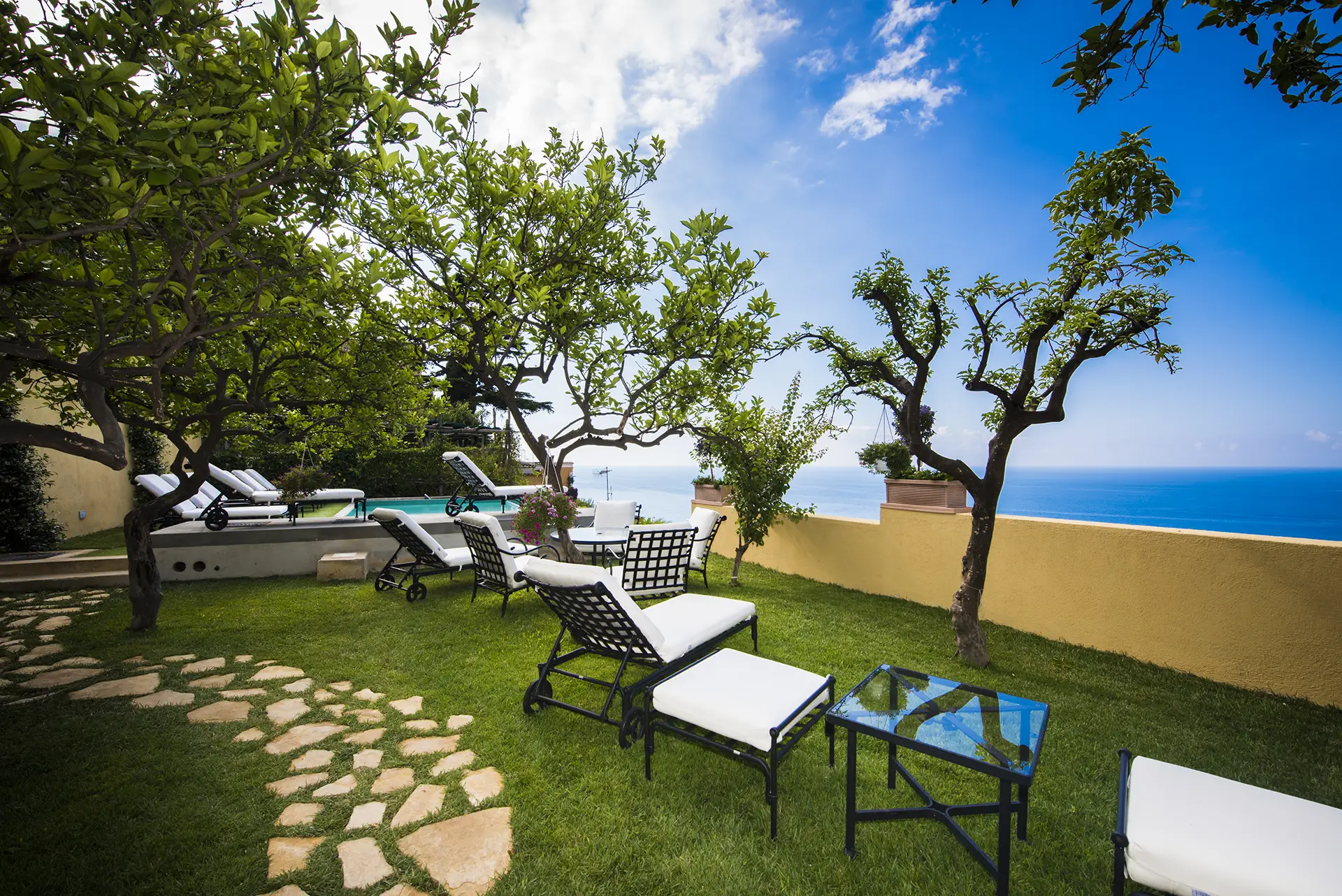 Giardino con lettini e vista sul mare sotto un cielo azzurro.