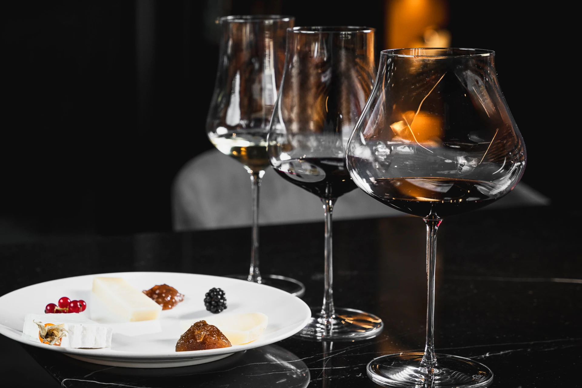 Tre calici di vino su un tavolo accanto a un piatto con formaggi e frutta.