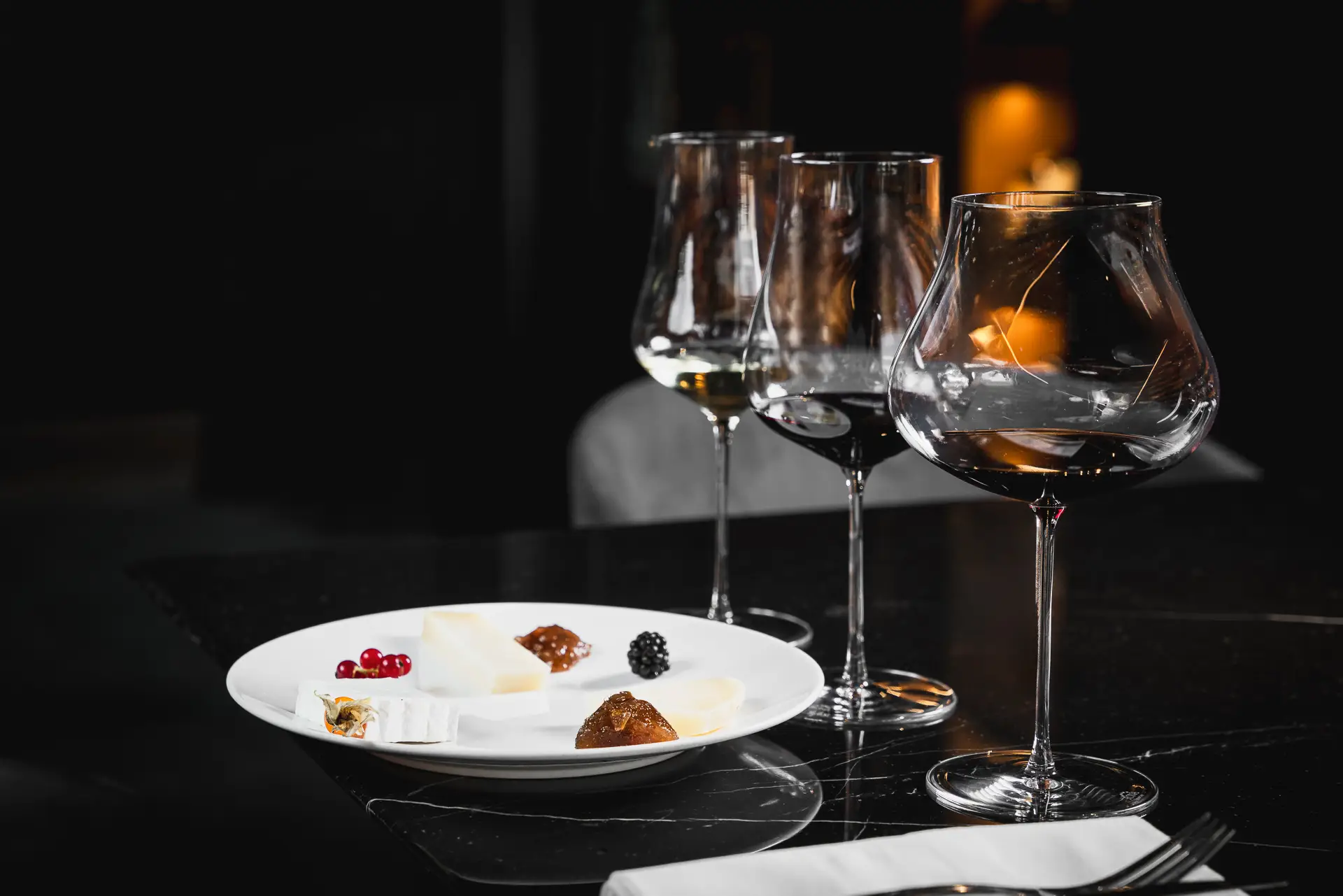 Piatto di formaggi e frutti su un tavolo elegante accanto a calici di vino.