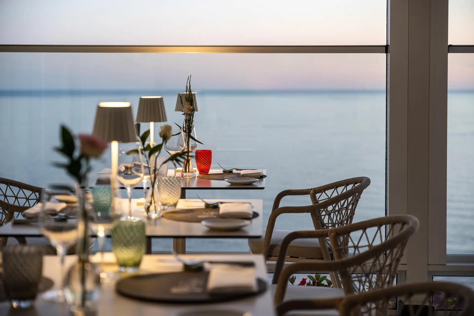 Tavoli elegantemente apparecchiati in un ristorante con vista sul mare al tramonto.