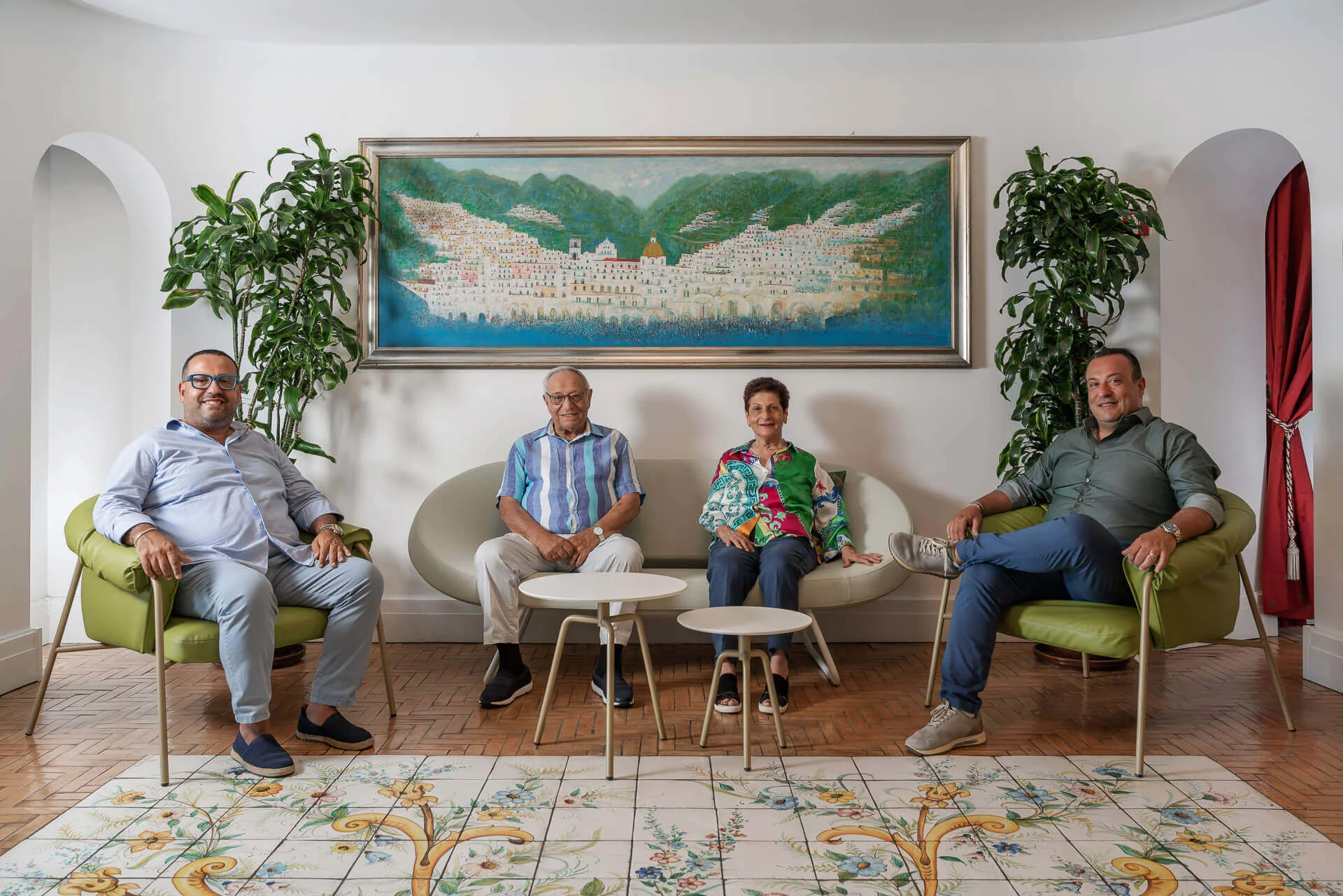 Quattro persone sedute in un salotto con un grande quadro e piante sullo sfondo.